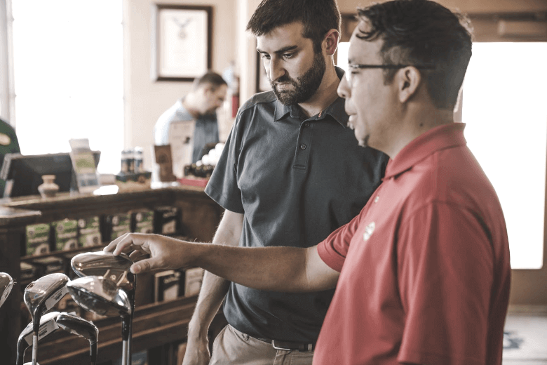 A golfer takes advice from store owner to choose his golf club and how to clean it